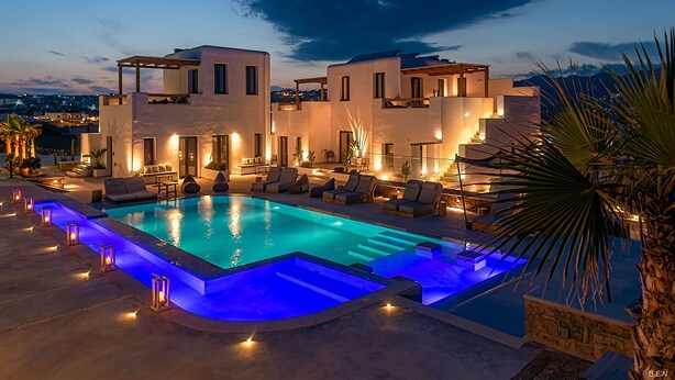 A modern poolside area with a swimming pool, lounge chairs, and a well-lit building in the background. - Le Palme Mykonos (Mykonos)