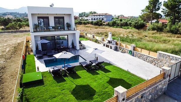 A modern two-story house with a swimming pool, outdoor seating, and a stone retaining wall. - Sun White Villa (Zakynthos)