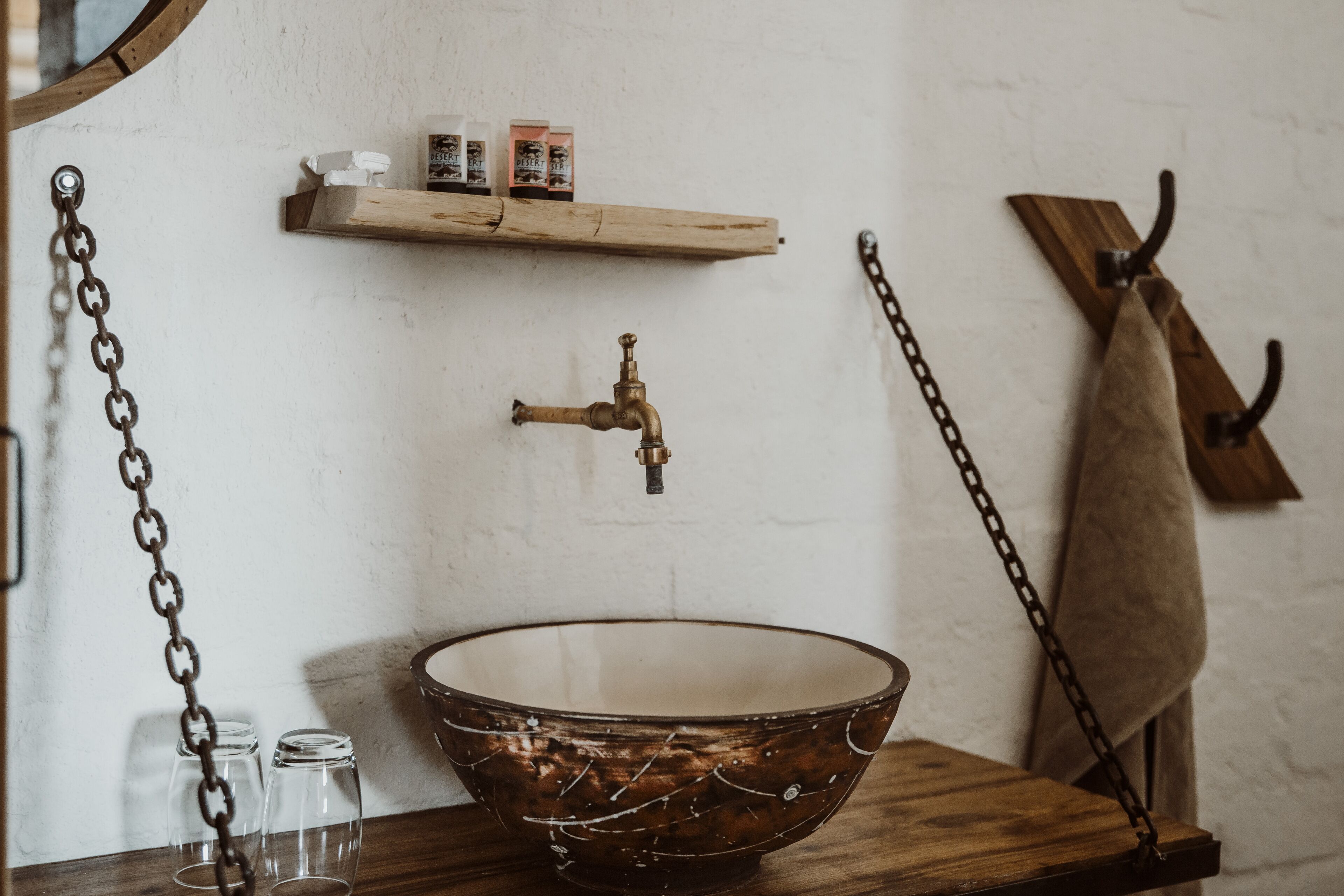 A rustic bathroom with a wooden basin, a vintage faucet, and a shelf with toiletries.
