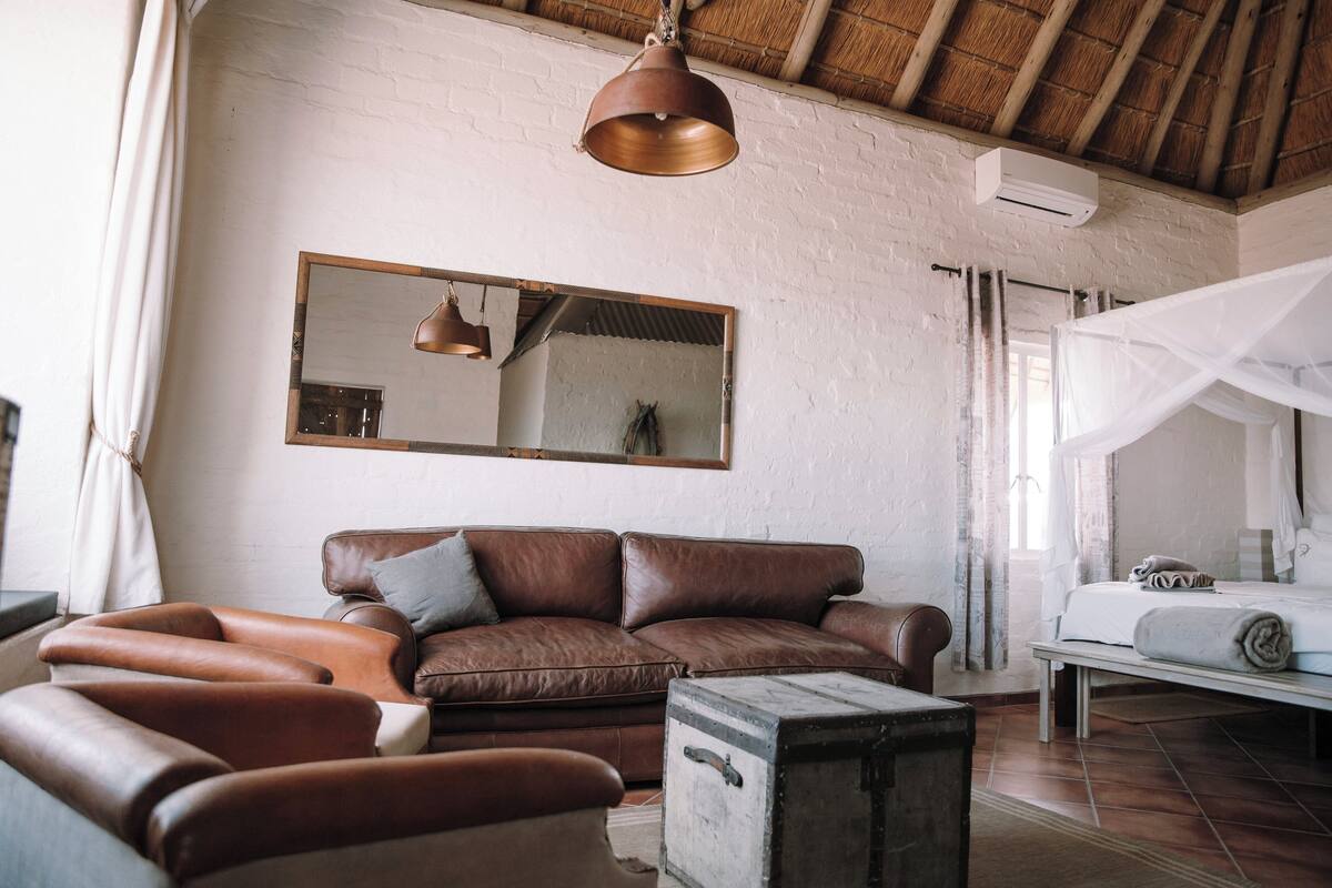 A cozy living room with a brown leather sofa, a wooden chest, and a bed with a canopy.