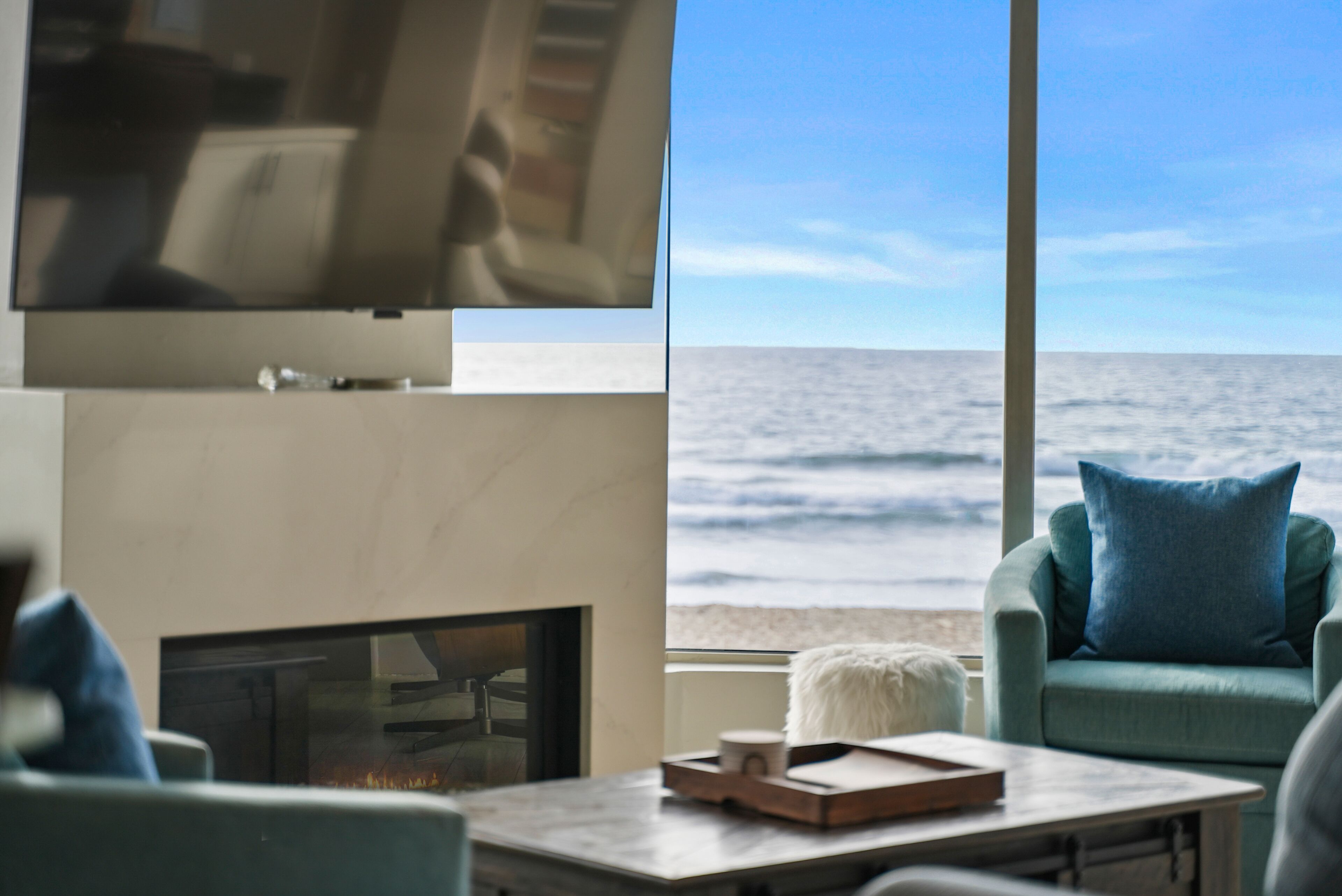 A modern living room with a fireplace, a flat-screen TV, and a view of the ocean.