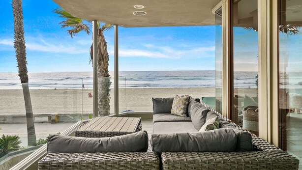 Ein Balkon mit einer Rattan-Couch und einem Tisch, mit Blick auf einen Strand mit Palmen und den Ozean.