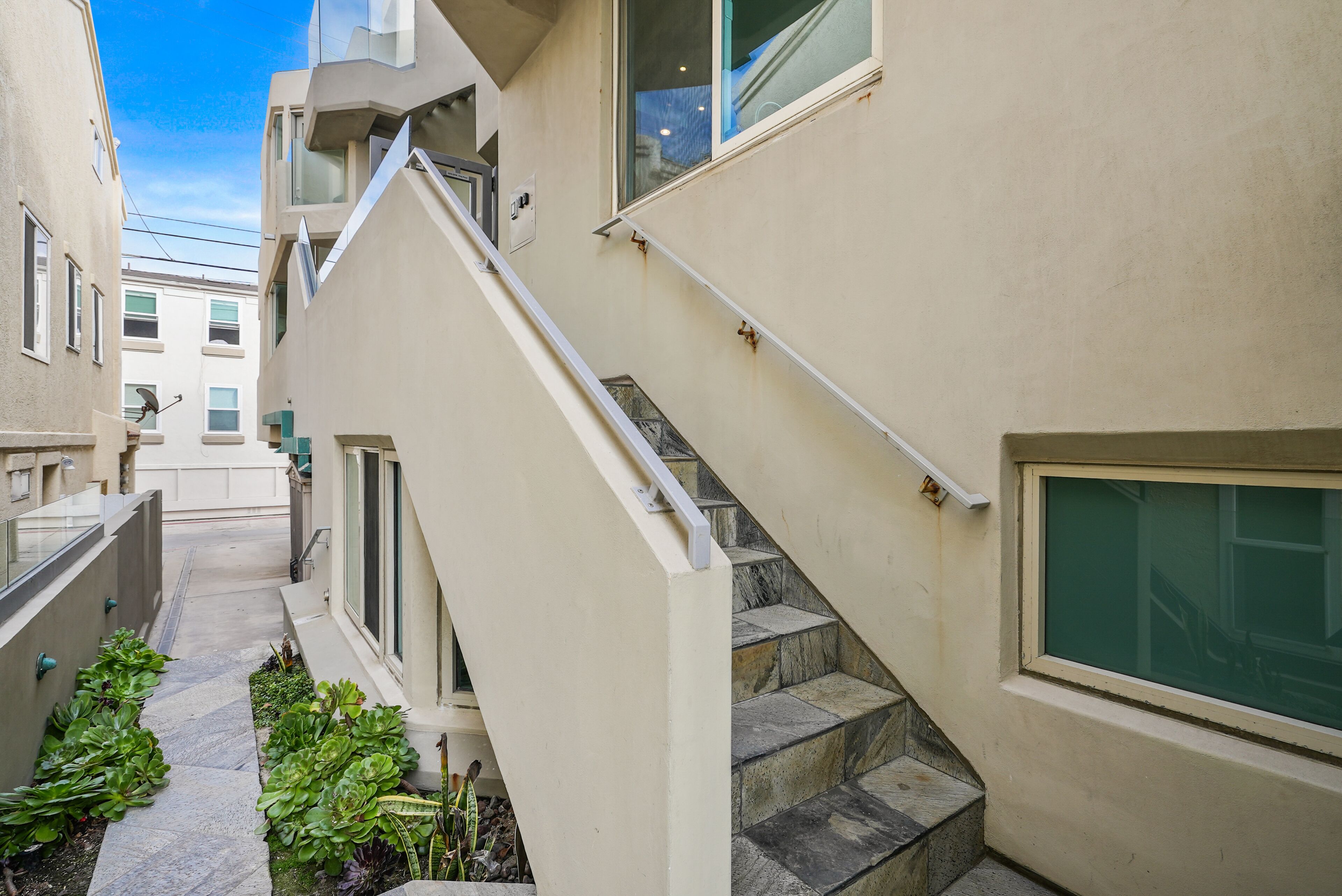 A narrow pathway leading to a set of stone steps with a white handrail.