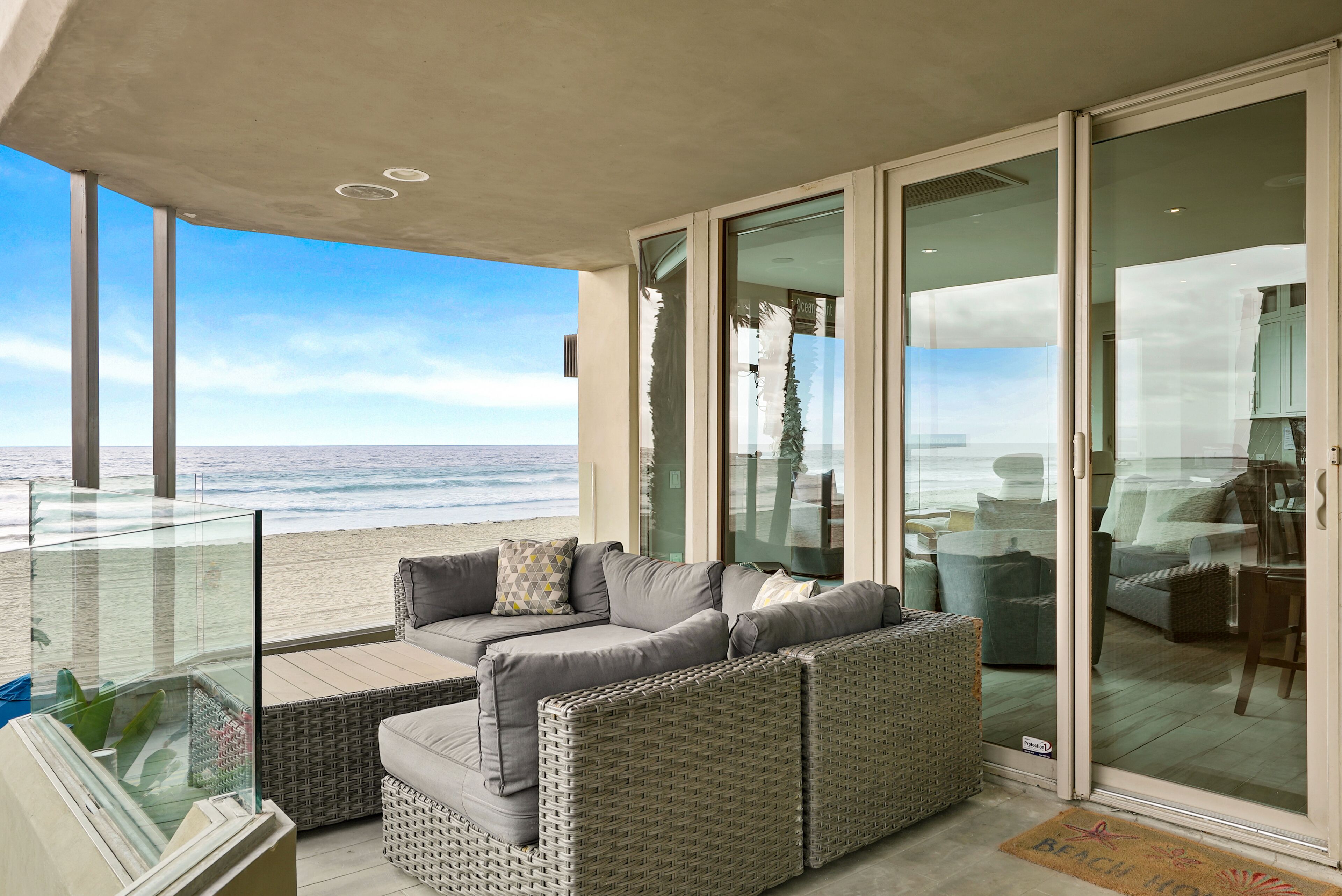 A balcony with a sofa and wicker chairs, overlooking a beach.