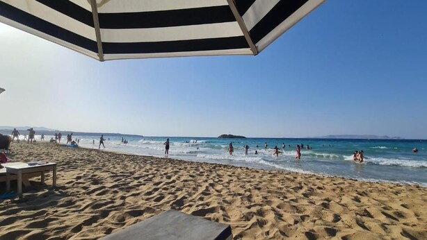 Une plage avec un parasol à rayures, du sable et des gens dans l’eau.