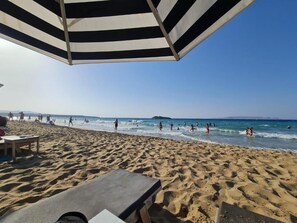 Uma praia com um guarda-sol listrado, areia e pessoas na água.