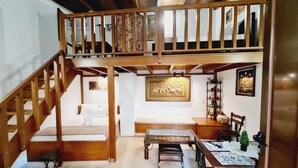 Une pièce spacieuse avec un plafond haut, un escalier en bois, un lit, une table à manger avec des chaises et un banc.