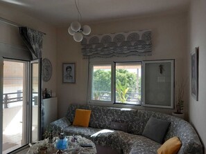 Un salon comprenant un canapé, une table agrémentée d’objets décoratifs, une horloge et une fenêtre donnant sur un paysage verdoyant.