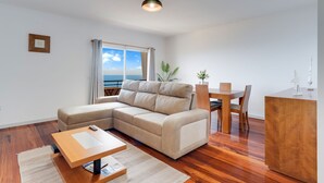 A modern living room with a sectional sofa, a wooden dining table, and a view of the sea through large windows. - Santa Cruz Apartment (Santa Cruz)