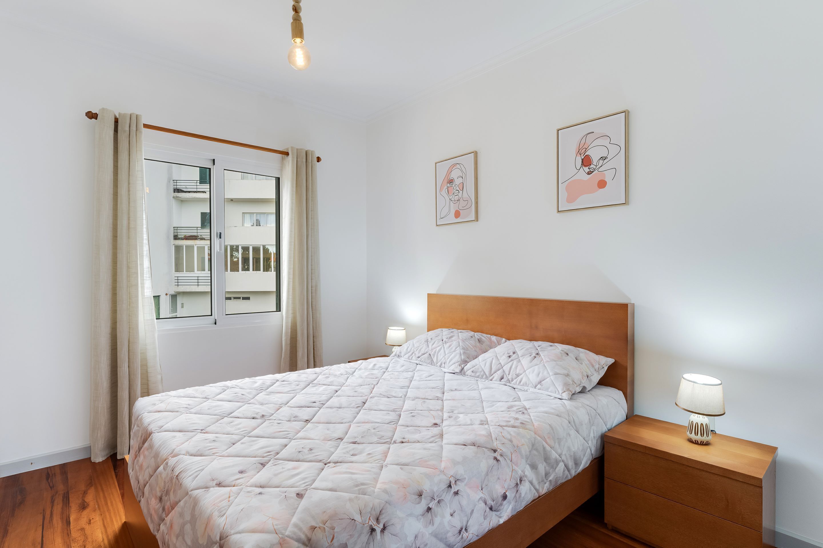 A bedroom with a bed, nightstands, a window with curtains, and wall art.