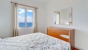 A bedroom with a bed, a wooden dresser, a window with curtains, and a mirror on the wall. - Santa Cruz Apartment (Santa Cruz)