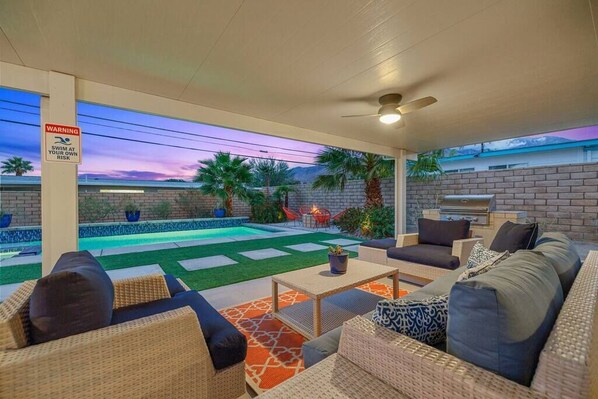 A covered outdoor area with a pool, seating, and a barbecue grill.