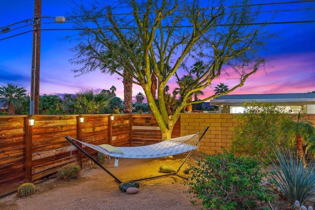 A hammock in a backyard with a wooden fence, a tree, and a brick wall.