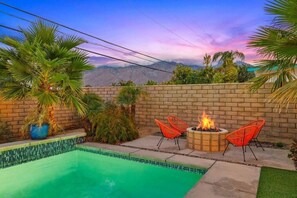 A backyard with a swimming pool, a fire pit, and outdoor seating.