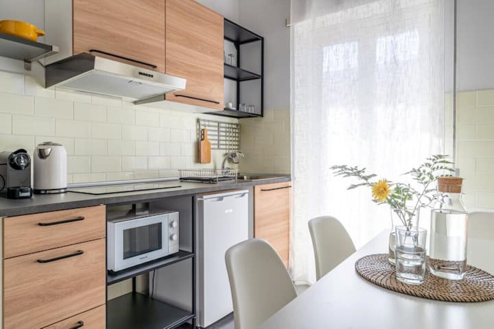 A modern kitchen with wooden cabinets, a microwave, a small refrigerator, and a dining area with a table and chairs.