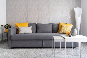 A modern living room with a grey sofa, yellow and white cushions, a white side table, and a tall white vase. - Bella Villa Road (Roma)