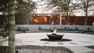 A circular outdoor seating area with a fire pit in the center, surrounded by a white floor and gravel.