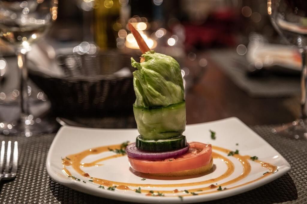 A plated dish with a vegetable roll, tomato slice, and sauce.