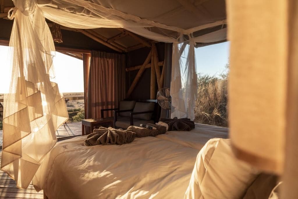 Una cama con dosel, una silla y una mesita en una habitación con vistas al exterior.