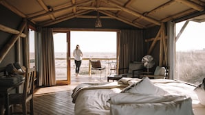 Ein Zimmer mit Bett, Ventilator, Tisch und Blick auf den Strand.