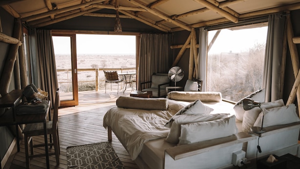 Ein gemütliches Zimmer mit einem großen Bett, einem Schreibtisch und einem Stuhl. Ein Fenster mit Vorhängen bietet Blick ins Freie.