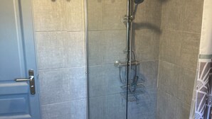 Un espace douche doté d’une porte en verre, d’un pommeau de douche et d’un panneau de commande.