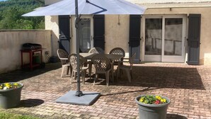 Une terrasse avec une table et des chaises, un parasol blanc et des plantes en pot.