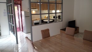 Un coin repas avec une table et des chaises en bois, une cuisine visible à travers une cloison en verre et un réfrigérateur.