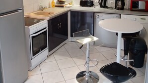 Une cuisine moderne avec des meubles en bois, un plan de travail blanc, un grille-pain noir, une machine à café et une table ronde blanche.