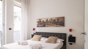 A neatly made bed with white linens and patterned pillows, a cityscape painting on the wall, and a small TV mounted on the wall. - Groovy Apartment: nice, modern and quiet house in the heart of Milan - 4 guests  (Milano)
