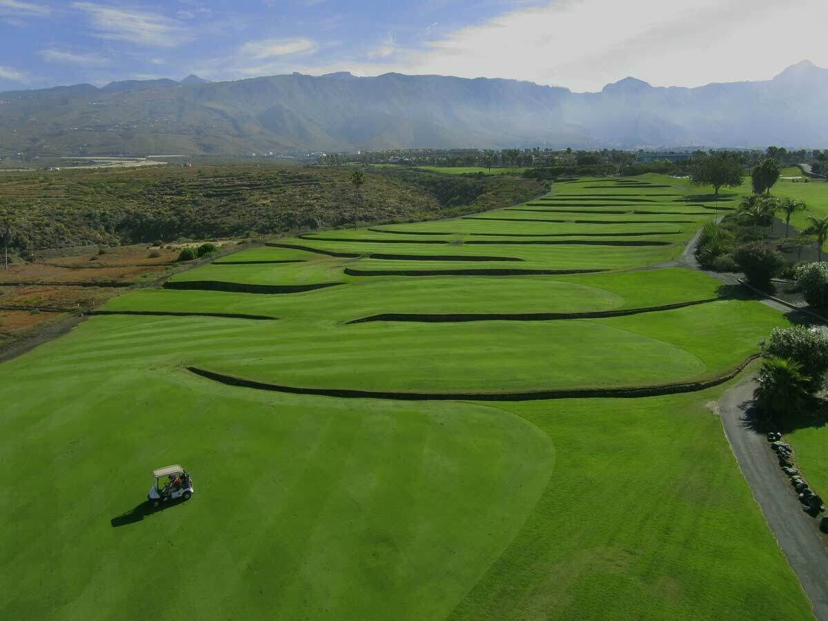 Un parcours de golf avec des voiturettes, entouré de montagnes et de verdure.