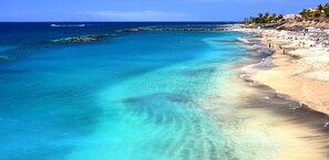 A beach with clear turquoise water, a sandy shore, and a rocky breakwater.