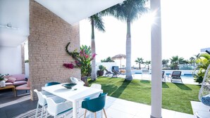 A patio area with a white table and chairs, a brick wall, and a view of a swimming pool and palm trees. - Elegant Villa with private pool and ocean view (CN)