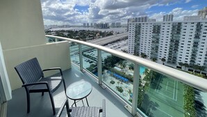A balcony with two chairs and a small table, overlooking a cityscape with high-rise buildings and a highway.