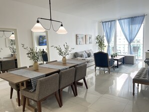 Een moderne woonkamer met een eethoek, met een bank, een salontafel en een eettafel met stoelen. Er staan potplanten en er hangt kunst aan de wanden.