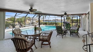 A covered patio with a glass table and chairs, overlooking a swimming pool and a view of a residential area.