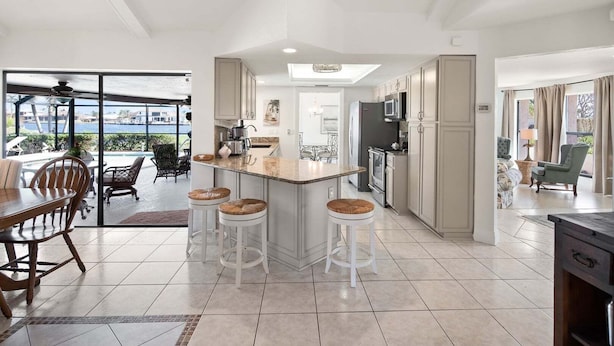 A modern kitchen with a central island, bar stools, and a dining area with a view.
