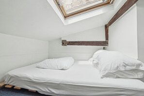 Een eenpersoonsbed met wit beddengoed in een kamer met witte wanden en een schuine plafond.