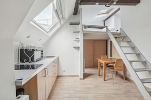Een compacte keuken met een inbouwfornuis, een zithoek met een houten tafel en stoelen, en een trap naar een verdieping.