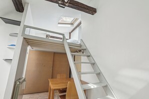 Een kamer met een hoogslaper, een houten tafel en een ladder.