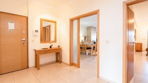 A spacious room with a wooden door, a wooden console table with a mirror, and a dining area visible through an open door.