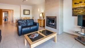 A modern living room with a leather sofa, a glass-top coffee table, a fireplace, and a TV.
