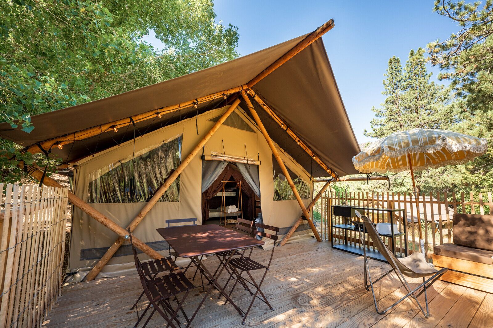 A tented accommodation with a wooden deck, a table, chairs, and an umbrella.
