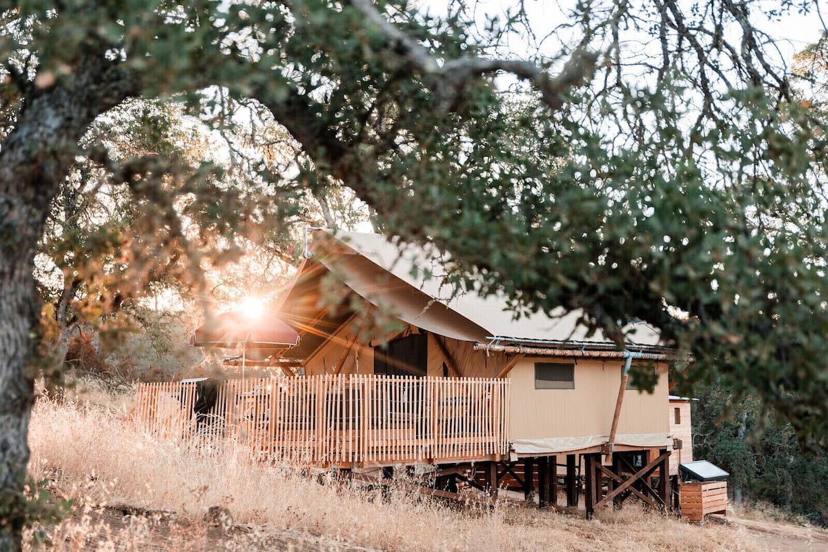 A rustic cabin with a wooden deck and a large tent-like structure.