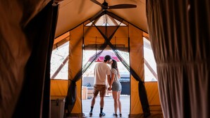 A couple standing at the entrance of a tent with a ceiling fan, a grill, and a view of the outside. - Huttopia Wine Country-Northern California (Lower Lake)