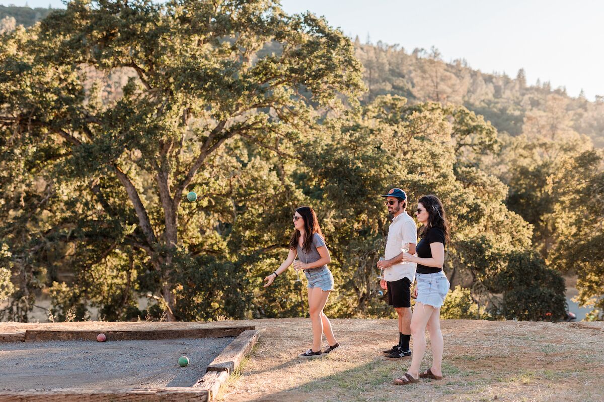 Un grupo de personas jugando croquet al aire libre, con árboles y colinas de fondo.