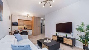 Una sala de estar moderna con un sofá, una mesa de centro, televisor y una cocina al fondo.