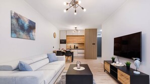 Una sala de estar moderna con sofá, mesa de centro, televisor y una cocina al fondo.