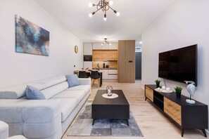 A modern living room with a sofa, coffee table, TV, and kitchen in the background.