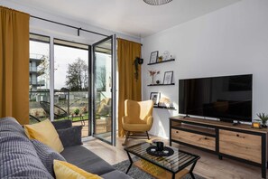 Un salon moderne avec un canapé, un fauteuil, un téléviseur et une table en verre.